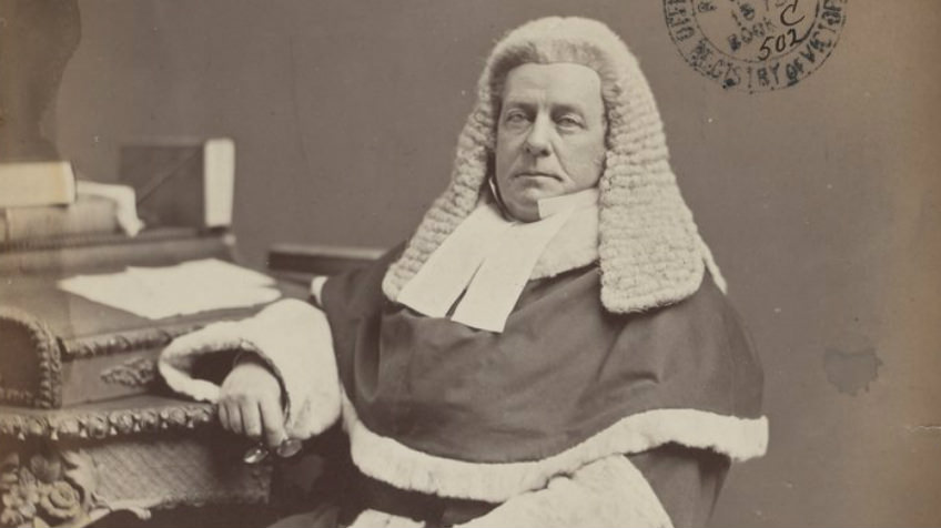 A grey scale image of a judge sitting down in his chambers