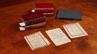 Image of rare books and pamphlets from the John Emmerson Collection at State Library Victoria placed on a brown table. There are five books and three pamphlets. 
