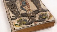 Close up image of a rare book with embroidered binding thought to belong to Queen Henrietta Maria, wife of King Charles I, from the John Emmerson Collection. The binding is ornate and detailed, and can be found across the entire book. The volume is placed on a white pillow.