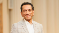 Headshot of State Library Victoria CFO and COO John Wicks. He is standing in the Ian Potter Queen's Hall and is wearing a light grey suit jacket with a white shirt.