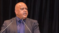 Close-up photograph of an Indigenous man wearing a suit standing at a lectern