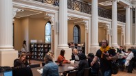 man walking past people at tables in grand hall with pillars