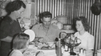 A black and white photograph of a family including a man, a woman and two children, gathered around a dinner table