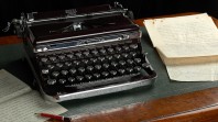 A manual typewriter sits beside typed pages on a leather-padded desk