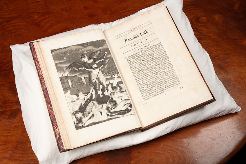 Image of opened rare edition of John Milton, Paradise lost, London, 1688 (first illustrated edition). The volume is placed on a white pillow on a brown table. On the left hand page is an illustration; on the right is the first page with headings stating Paradise Lost, Book 1.