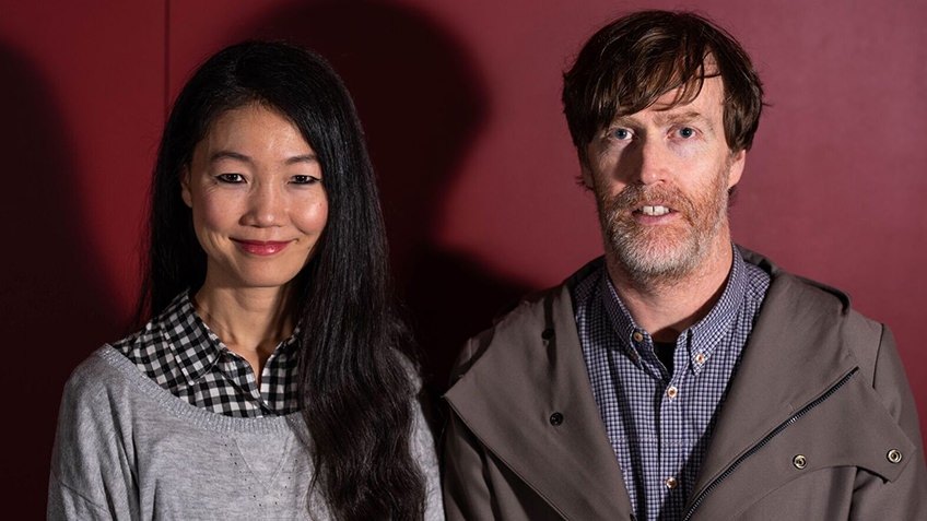 portrait of smiling woman with long dark hair and man with beard against red background