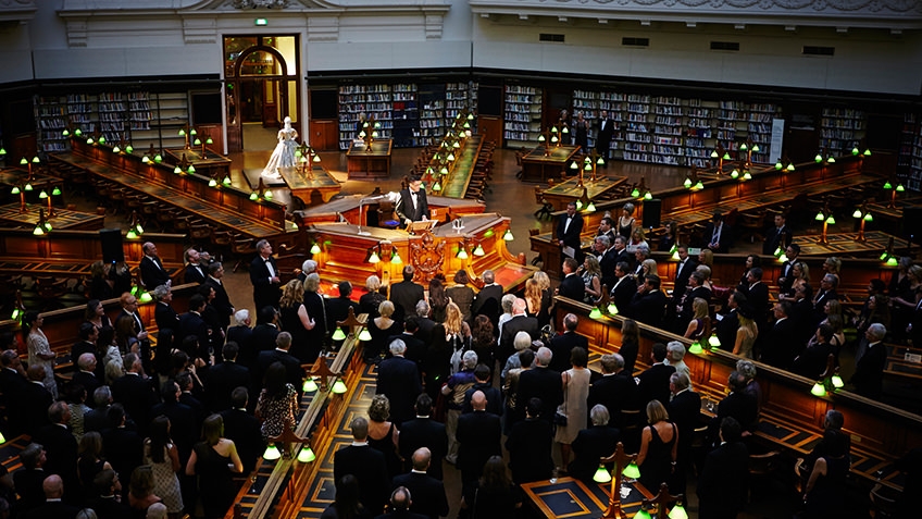 An evening performance in the La Trobe Reading Room for a standing audience in formal attire