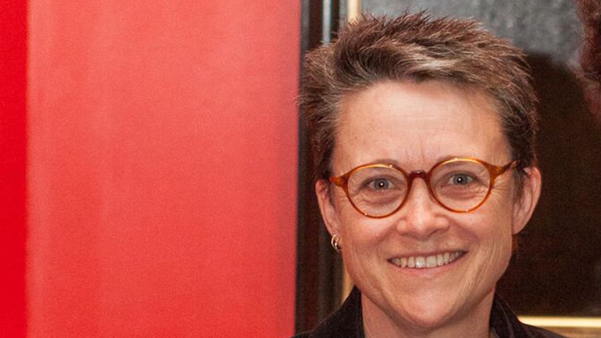 Woman with short hair and spectacles against a red background