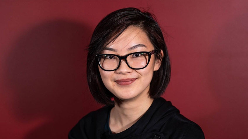 portrait of young woman with short dark hair with dark spectacles against red background