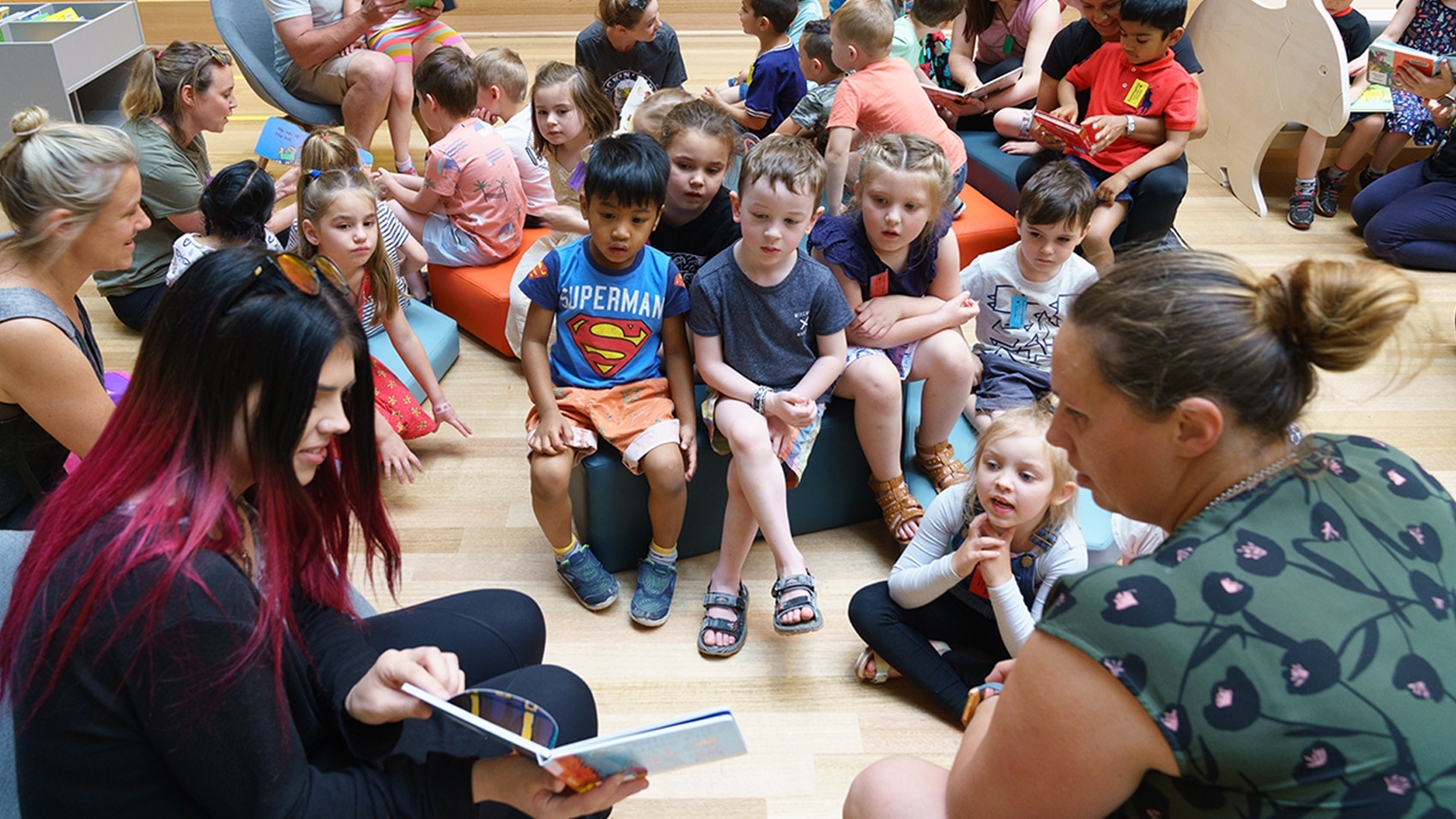 two women presenting a book reading to seated children