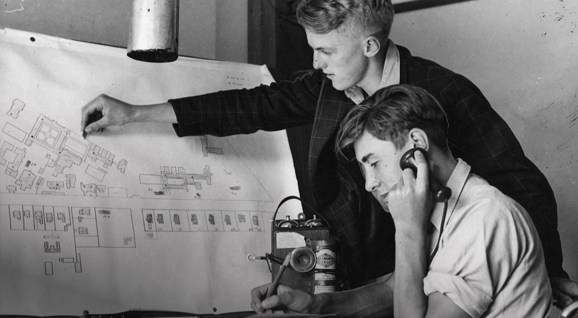 One boy points to a map while another listens on an old analogue phone