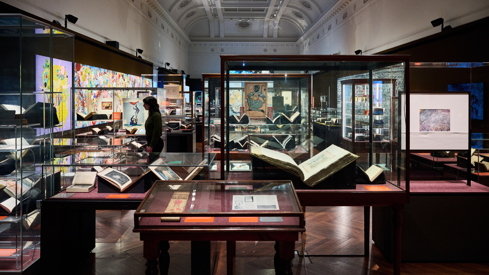 Installation view of Creative Acts: Artists and their inspiration at State Library Victoria. There are a number of cabinets and cases in the foreground featuring books and other items from the collection. It is a very full gallery.