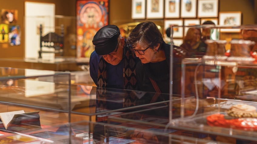 An elderly couple looking at a display case of items in Creative Acts exhibition