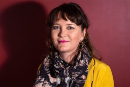 portait of woman with short hair wearing scarf and yellow jacket against red background