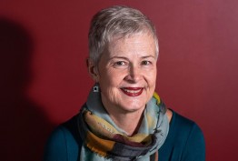 portrait of older woman wearing a scarf and teal jumper against red background