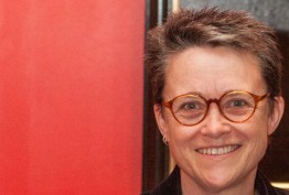 Woman with short hair and spectacles against a red background
