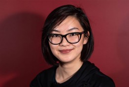 portrait of young woman with short dark hair with dark spectacles against red background