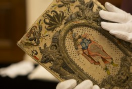 Colour photo of gloved hands holding colourfully embroidered historic binding thought to belong to Queen Henrietta Maria, wife of King Charles I, c1630