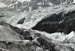 Black and white photo of small group of mountaineers ascending snow covered alps, possibly in Switzerland, carrying walking sticks or mountain poles