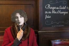 french cafe with blackboard menu and woman in red coat holding up the black and white facemask of a woman