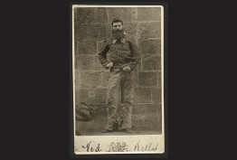 black background with sepia photo of bearded man in chains against bluestone wall