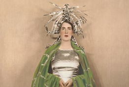 A woman in a vibrant hat and green cape