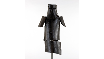 Photograph of Ned Kelly's suit of armour against a white/grey background. The armour has been installed on a metal pole.
