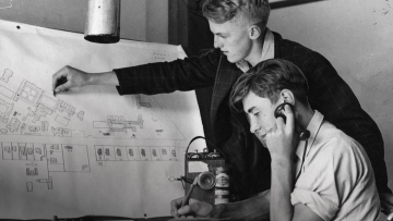 One boy points to a map while another listens on an old analogue phone