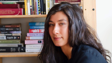 Author Didem Caia staring at the camera with a book shelf behind her. 