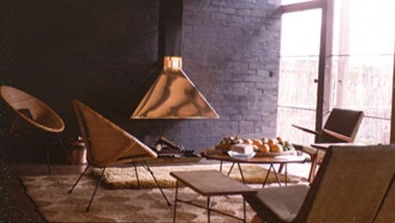 dark lounge room with light streaming in through glass doors, copper fireplace and modernists chairs
