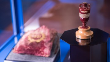 A small ceramic urn and velvet bag in an exhibition display case