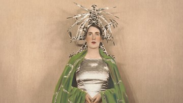 A woman in a vibrant hat and green cape
