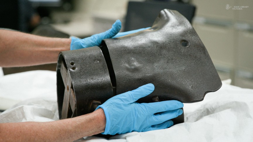 Two hands with blue gloves on holding a metal helmet