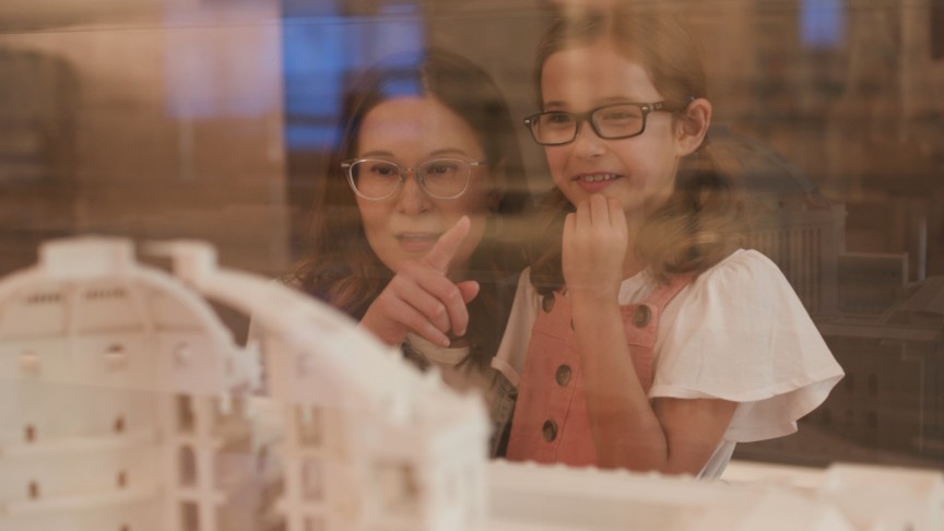 A woman and young girl peer through a window at a paper sculpture